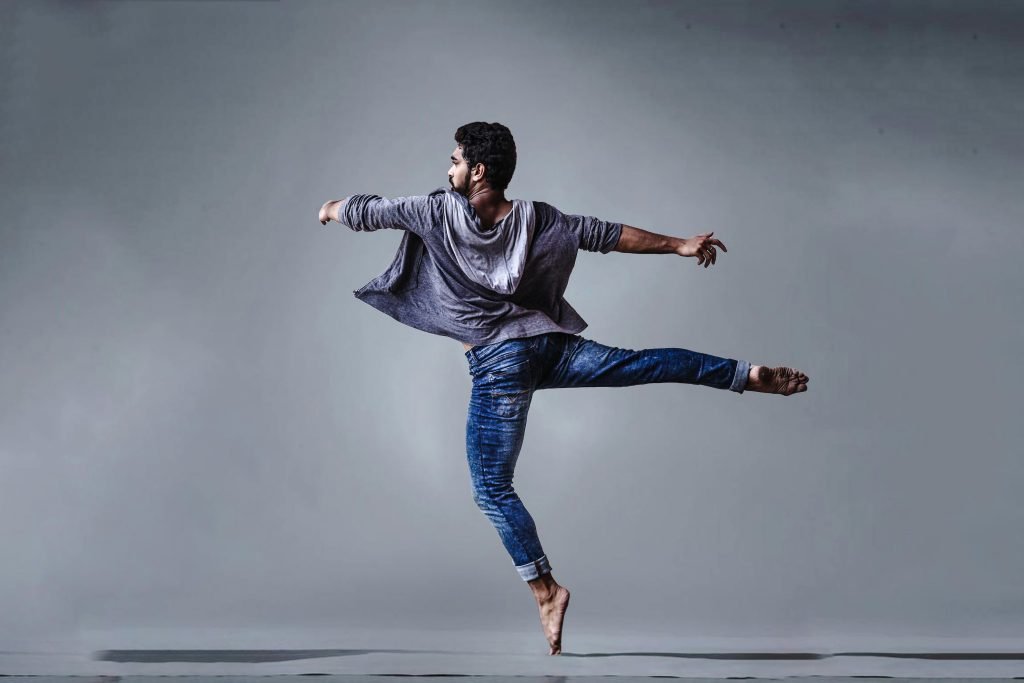 A male dancer executing a high jump in a studio setting, showcasing grace and agility.