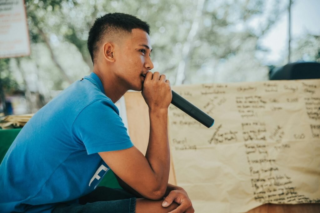 A young man in casual clothing speaks into a microphone outdoors in Calatagan, Philippines.