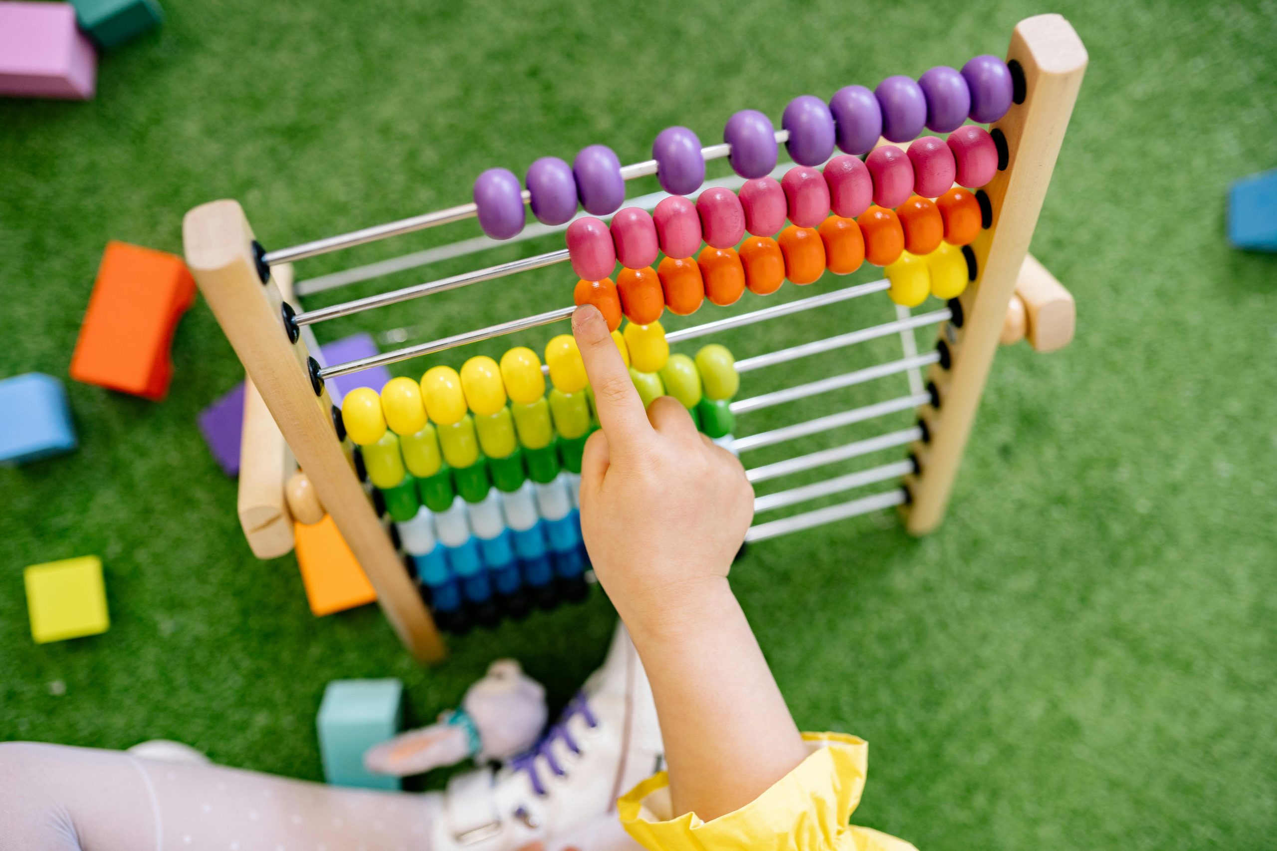 A child's hand using a colorful wooden abacus on green turf, emphasizing playful learning.